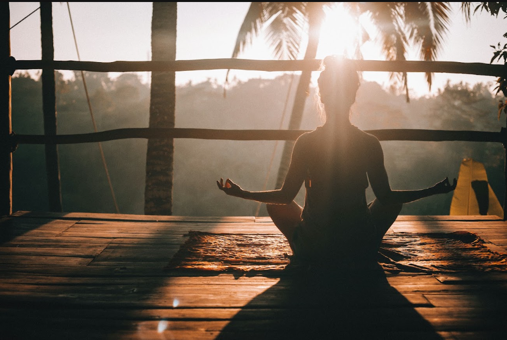 Person meditating at sunrise on an open-air wooden deck